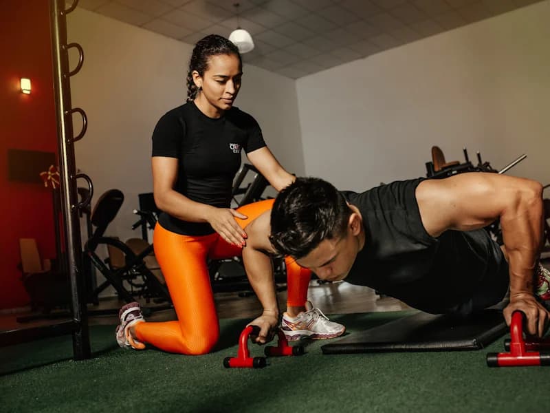 Trainer coaching a man doing push-ups on parallette bars in a gym