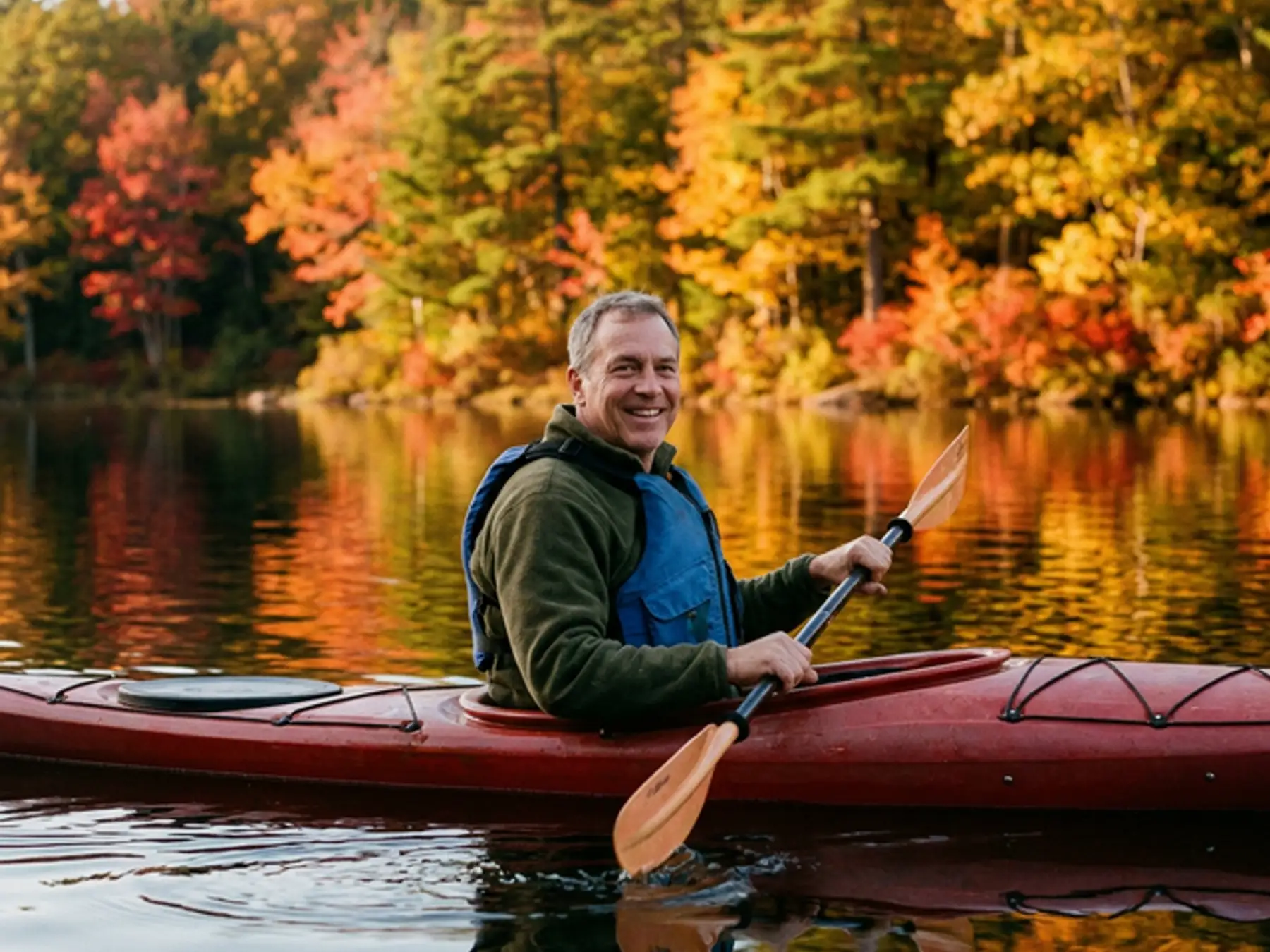 Man paddling a red kayak on a lake ringed by autumn foliage