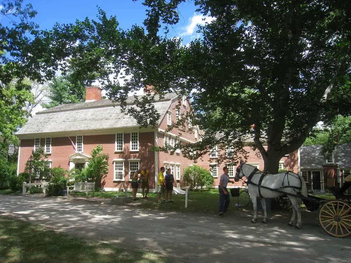 Longfellow’s Wayside Inn in Sudbury, Massachusetts — the historic low red wood-clapboard colonial inn with a white horse and carriage on the lawn beneath mature shade trees