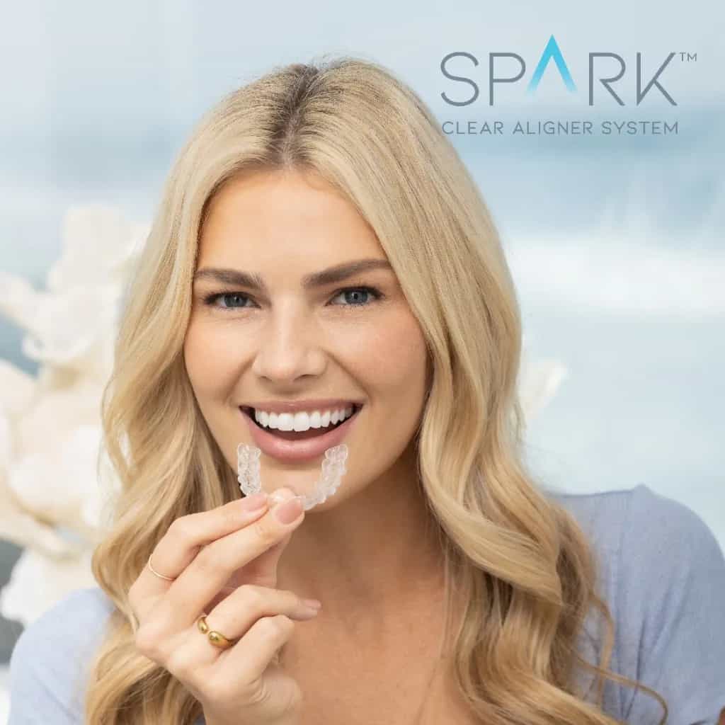 Smiling woman holding a set of Spark clear aligners